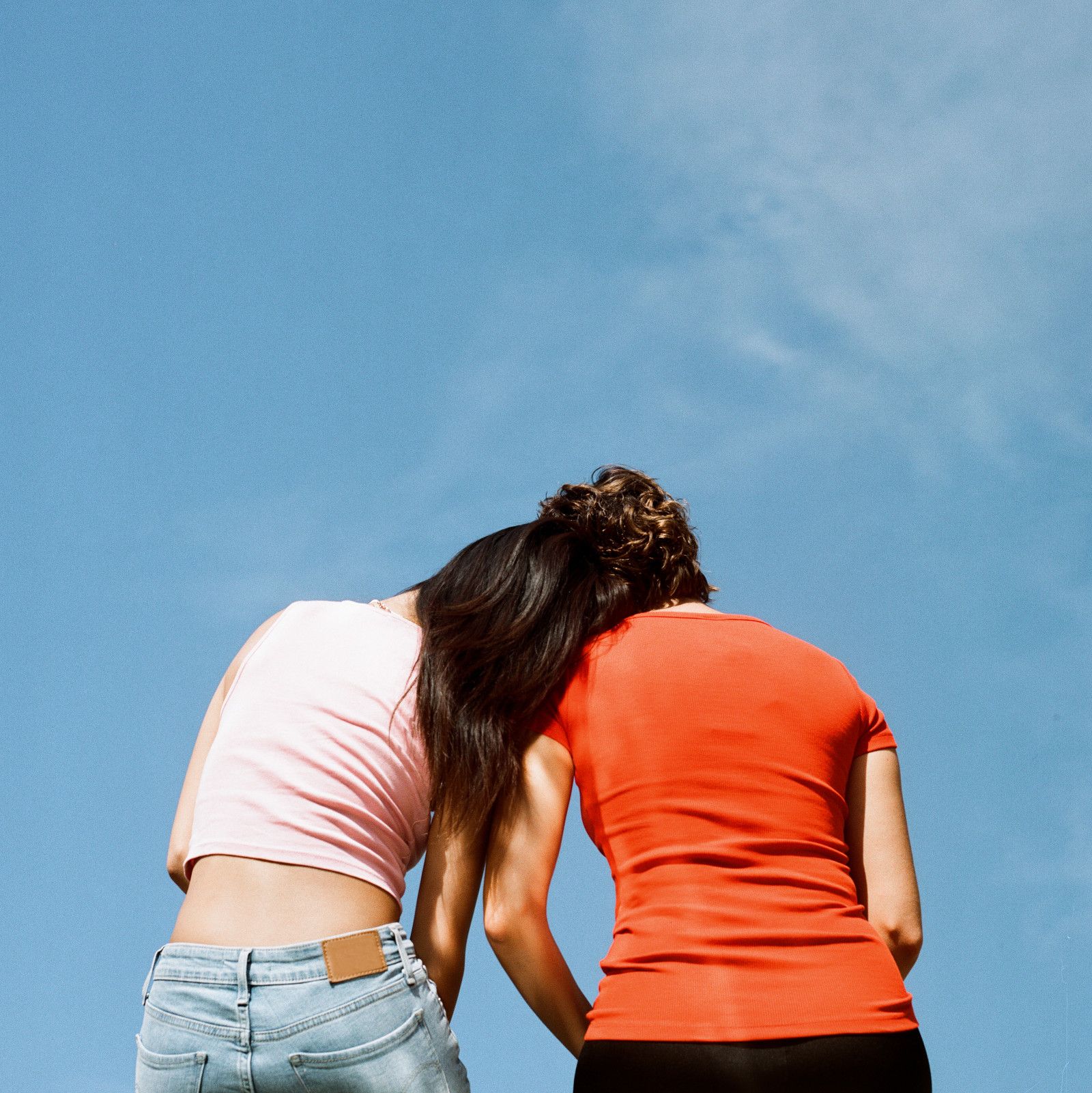 Dos personas de espalda con playeras de colores frente a un cielo azul