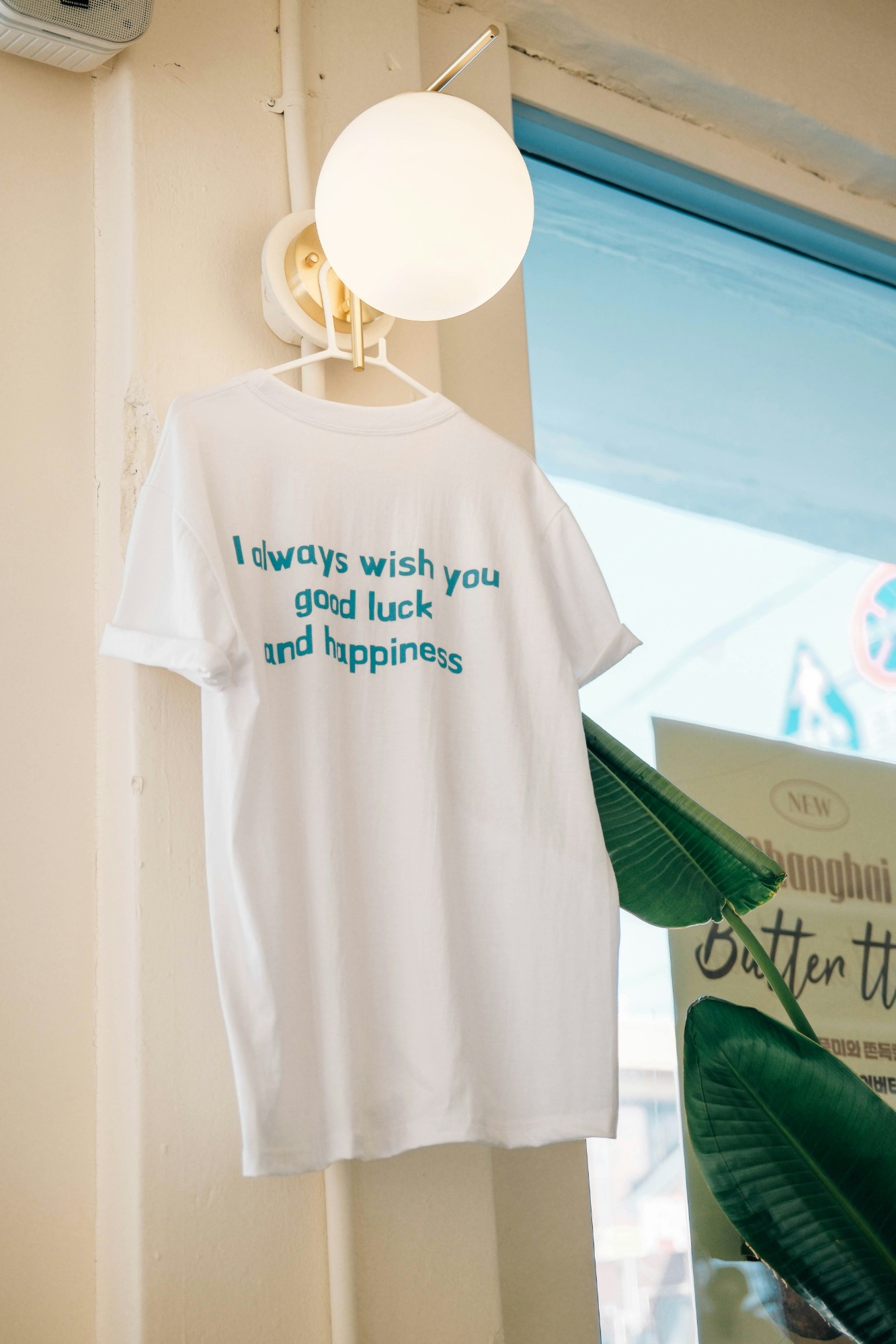 Playera blanca con estampado de texto azul colgada junto a una ventana